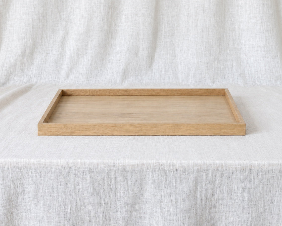 A rectangular light oak wood tray with a natural finish, displayed on a draped white linen fabric background.