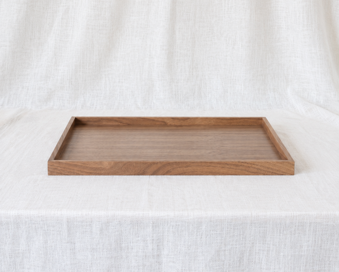 A rectangular wooden serving tray with a natural medium-brown finish and visible wood grain, displayed on a draped white linen fabric background.