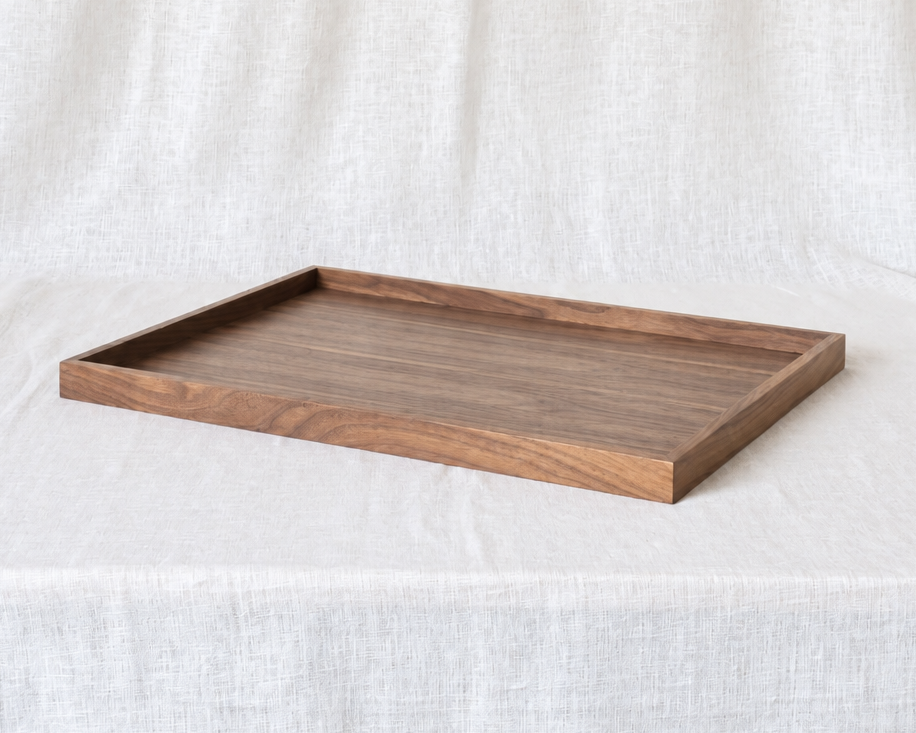 A rectangular wooden serving tray with a medium brown wood grain finish, displayed on a draped white linen fabric background.