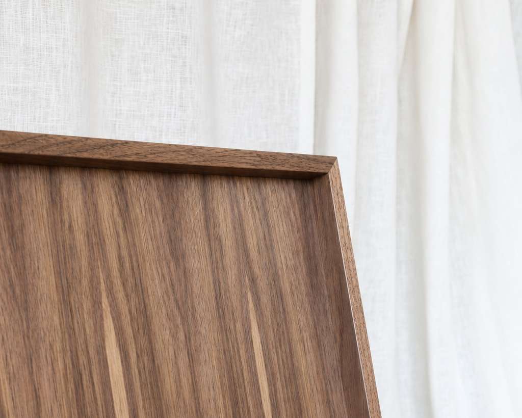 Close-up of a medium brown wood-grain tray corner with a white fabric curtain background.