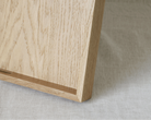 Close-up of a light natural wood tray corner resting on a textured off-white fabric surface.
