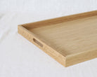 A light natural wood serving tray with a cutout handle, photographed on a white textured fabric background.