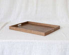 A rectangular wooden serving tray with two cutout handles on the sides, displayed on a draped white linen fabric background.