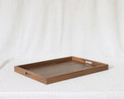 A rectangular wooden serving tray with two cutout handles, resting on a draped white fabric background.