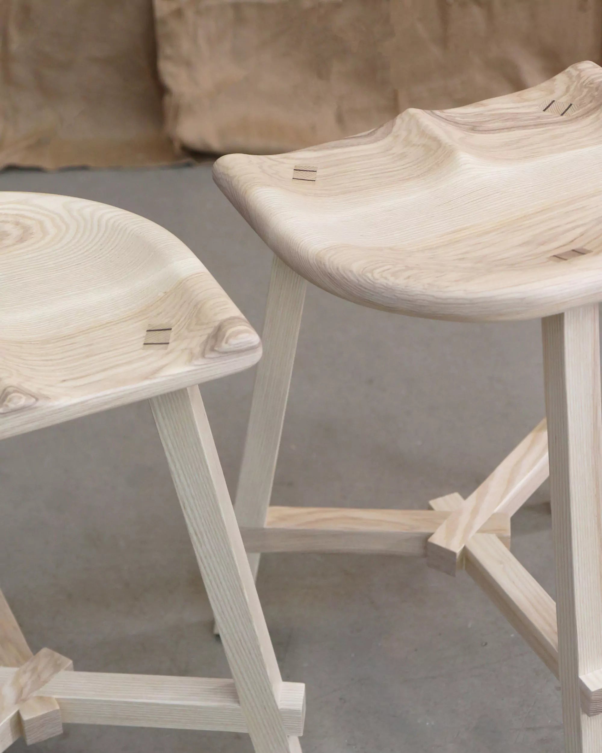 Two wooden stools with a natural finish on a gray floor.