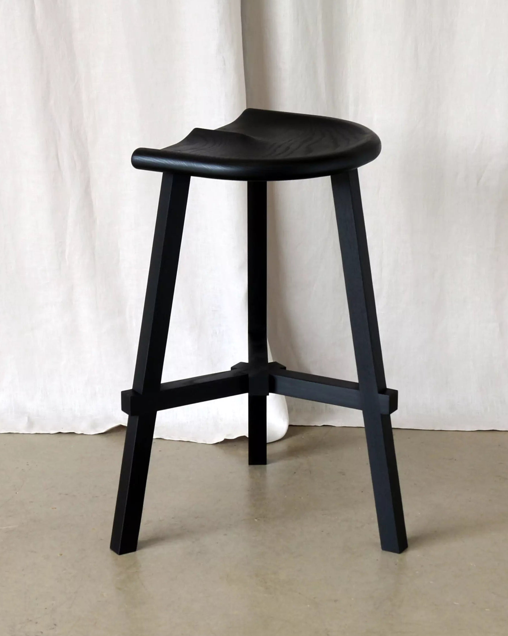 Black stool against a white curtain background