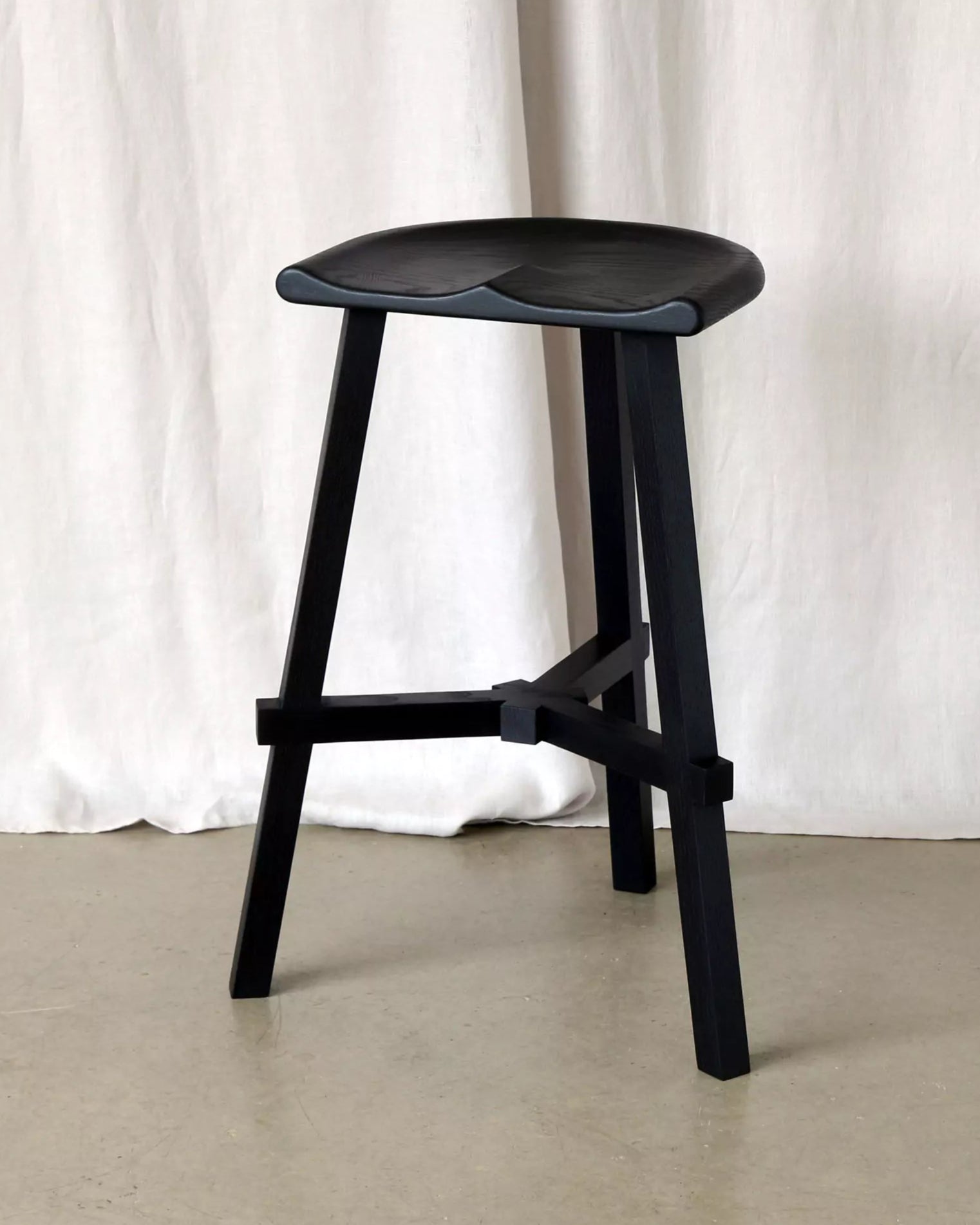 Black stool against a white curtain background