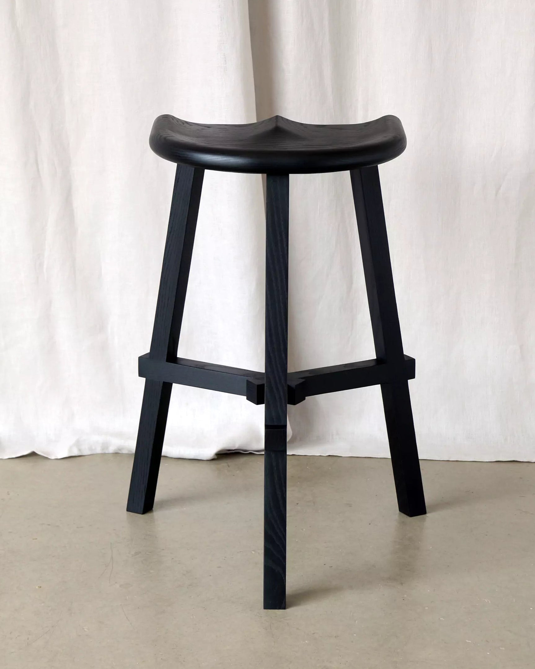 Black stool against a white curtain background