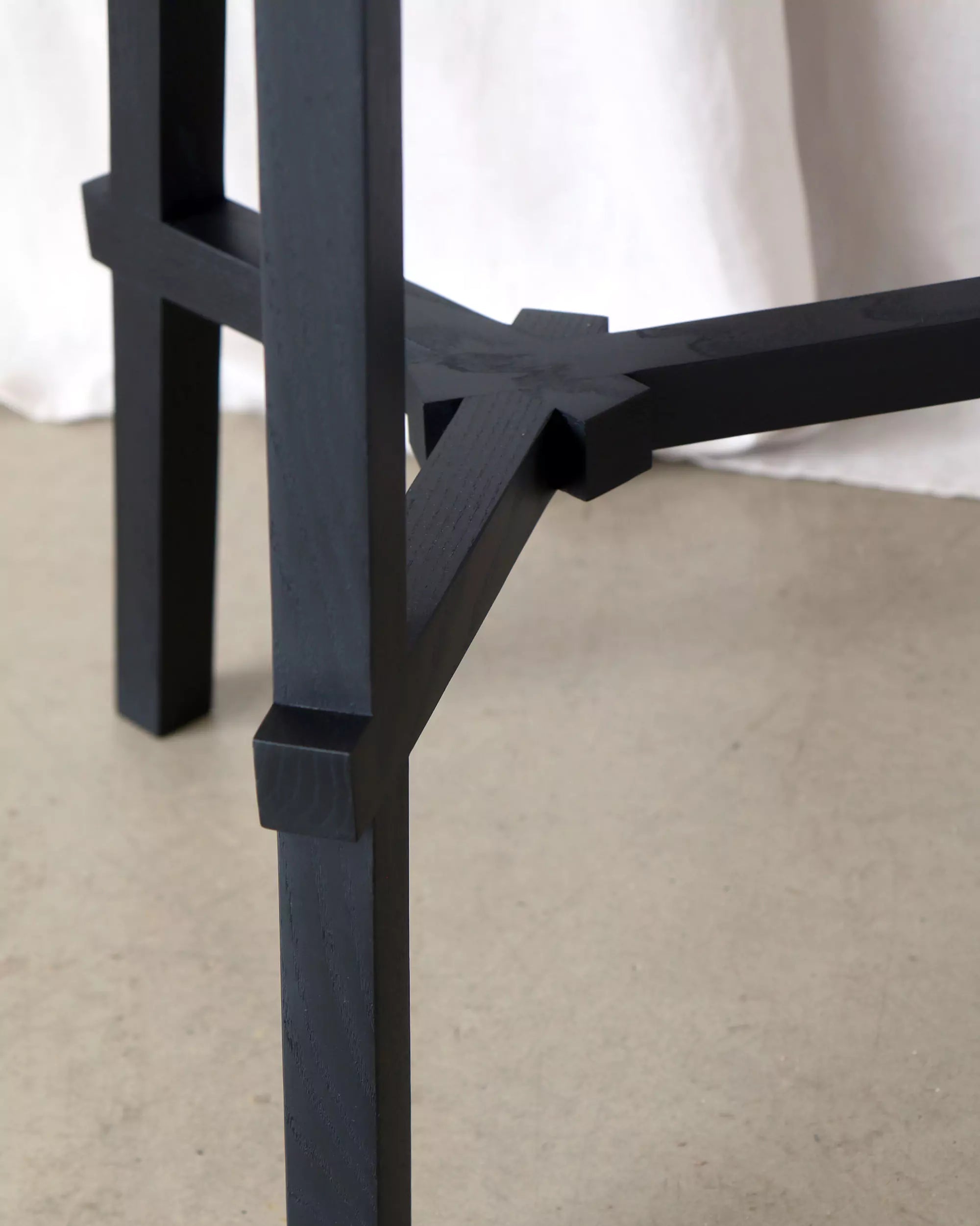 Close-up of a black wooden chair leg on a beige floor with a white curtain in the background.