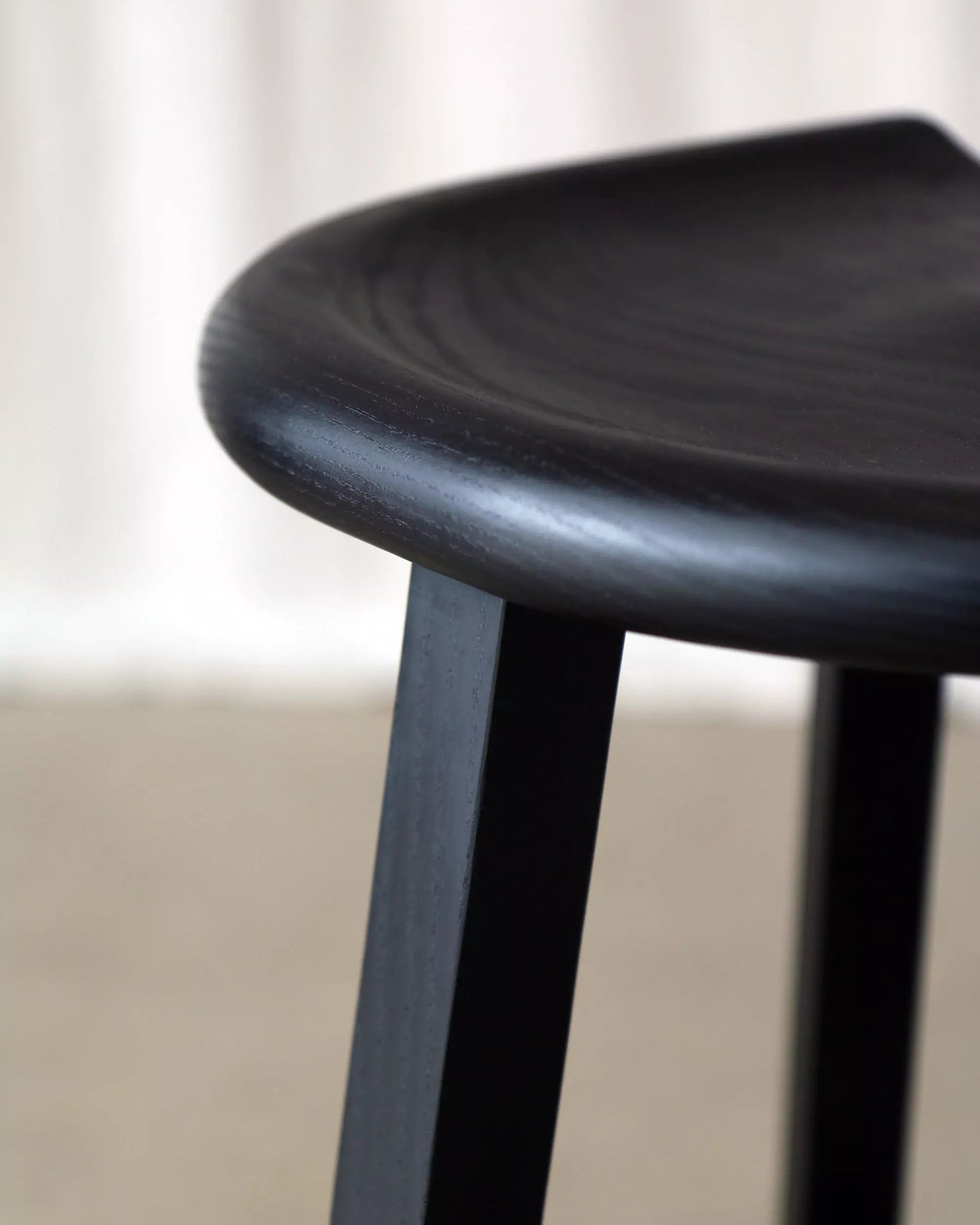 Close-up of a black stool with a carved seat and a  blurred background