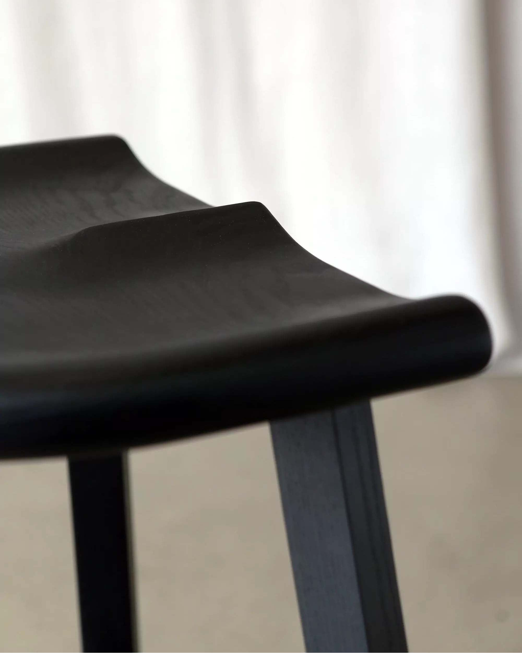 Black stool carved seat close-up with a blurred white curtain background