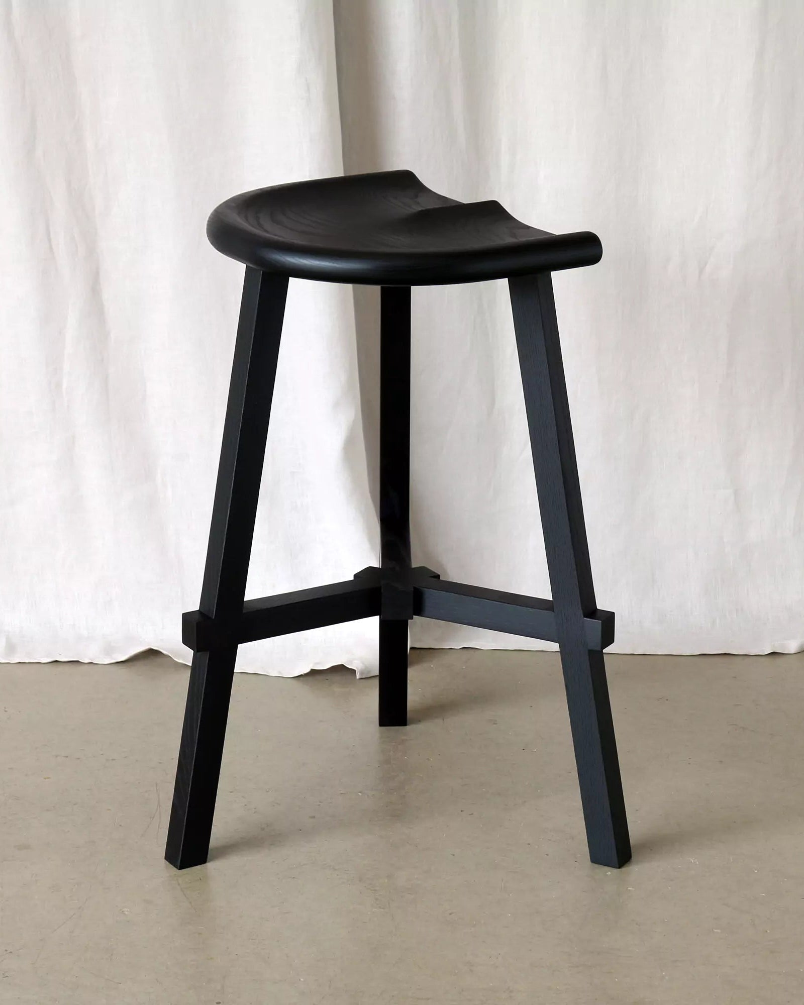 Black stool against a white curtain background