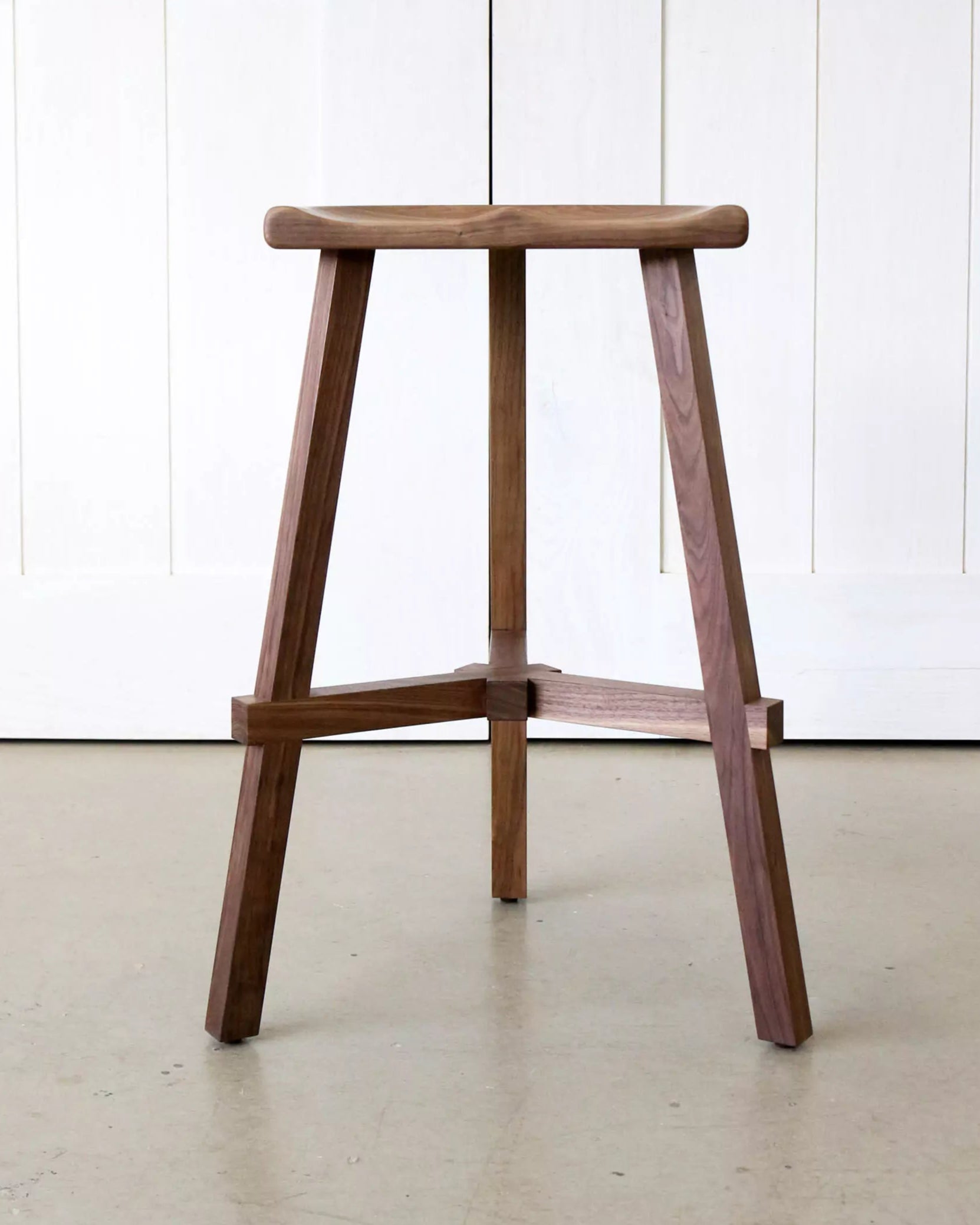 Wooden bar stool against a white paneled wall.