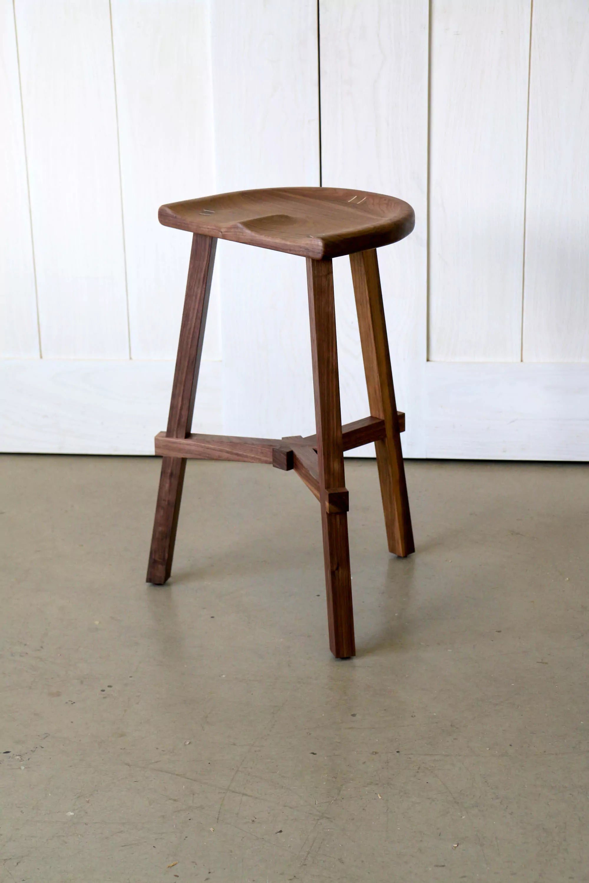 Walnut stool on a plain floor and white panelled wall background