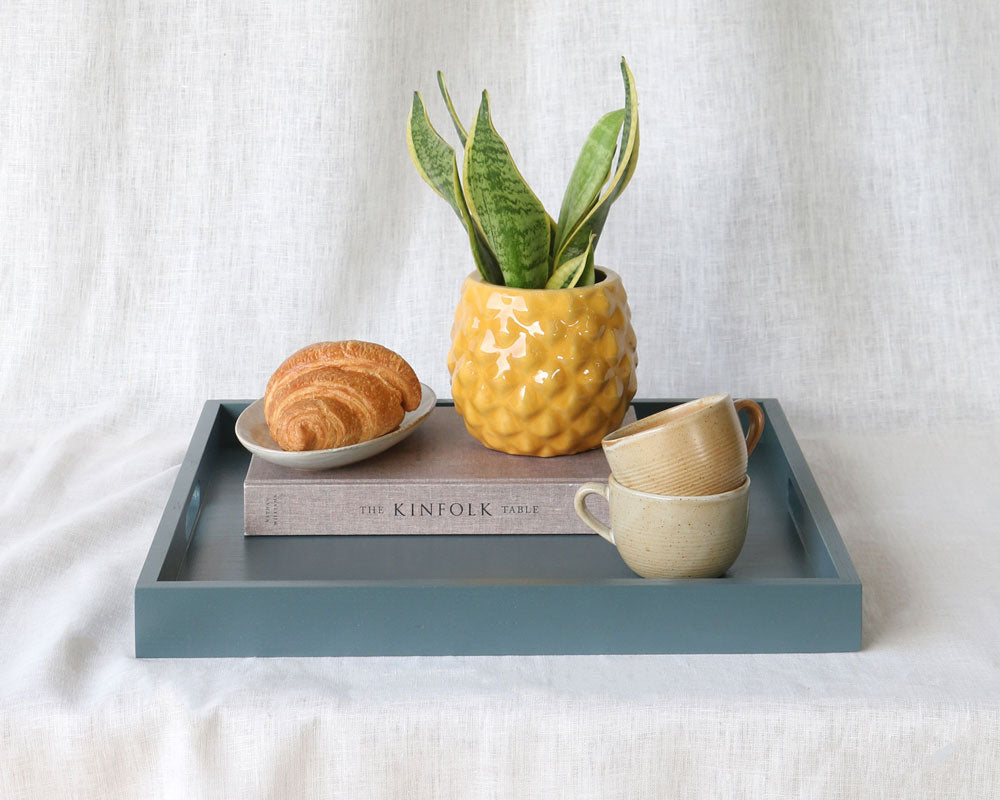 Styled tray with a yellow pineapple-pattern planter, stacked mugs, a croissant, and “The Kinfolk Table” book, with “More Colours Available” text and Martelo & Mo logo overlay.