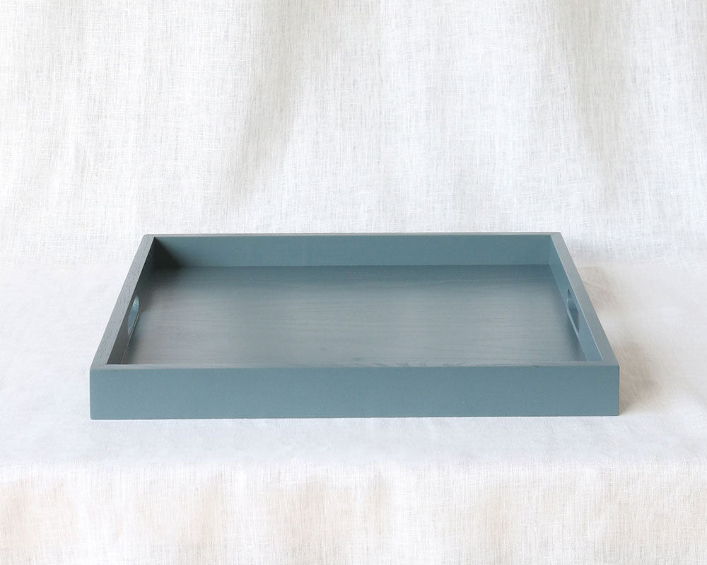 traight-on view of an empty blue-grey ottoman tray showing both handles, placed on a neutral fabric surface.