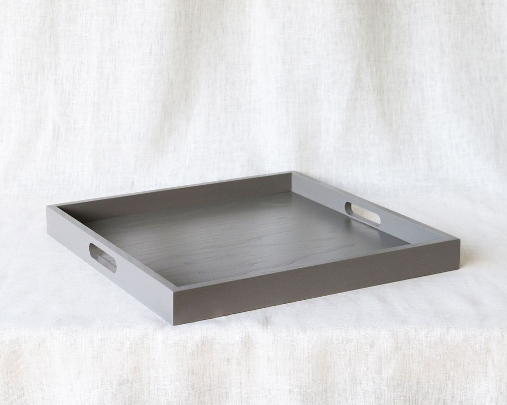 Side-angled view of a rectangular grey ottoman tray with both handles visible and wood texture slightly apparent.