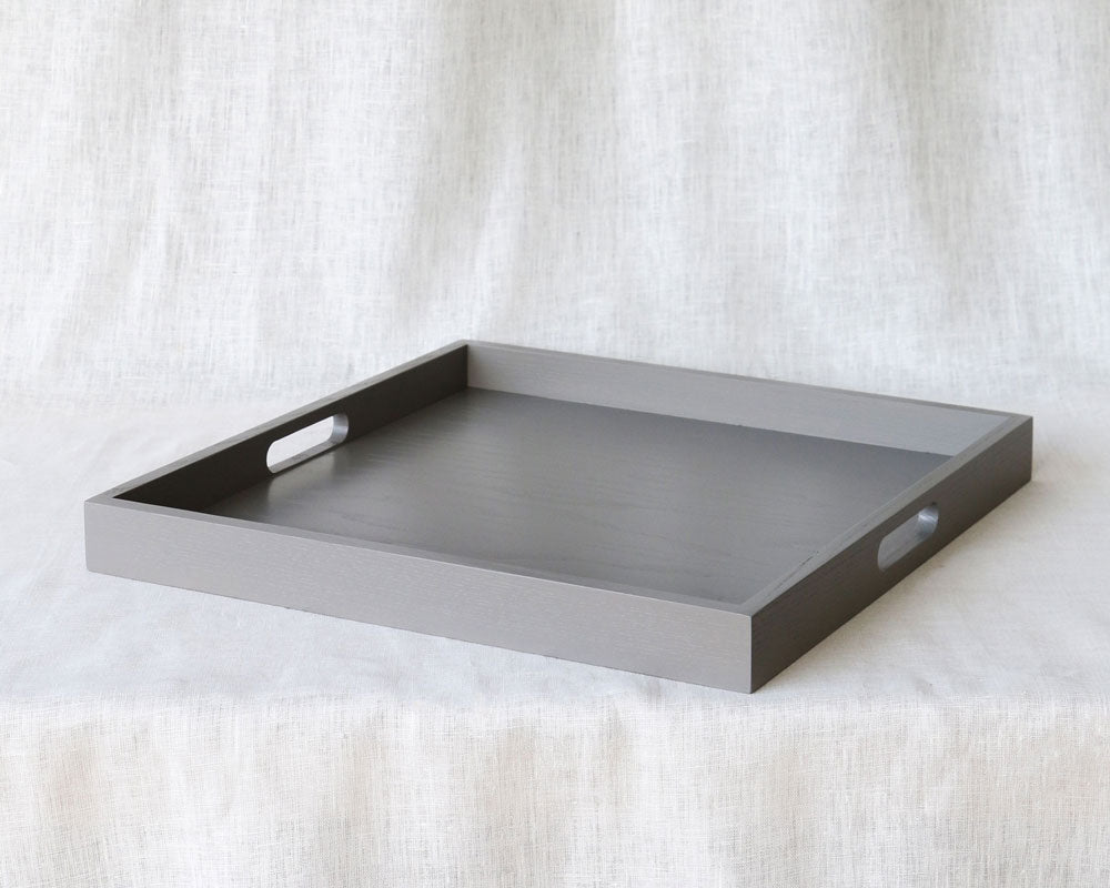 Wide-angle diagonal view of the grey ottoman tray with handles, placed on a soft fabric surface.