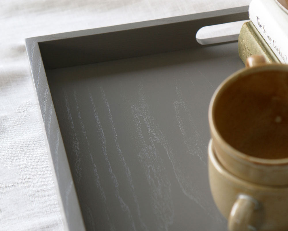 Angled view of the tray corner with visible wood grain and a ceramic cup partially shown in the frame.