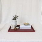 Wooden tray with decorative items including a mug, books, and a plant on a white surface.