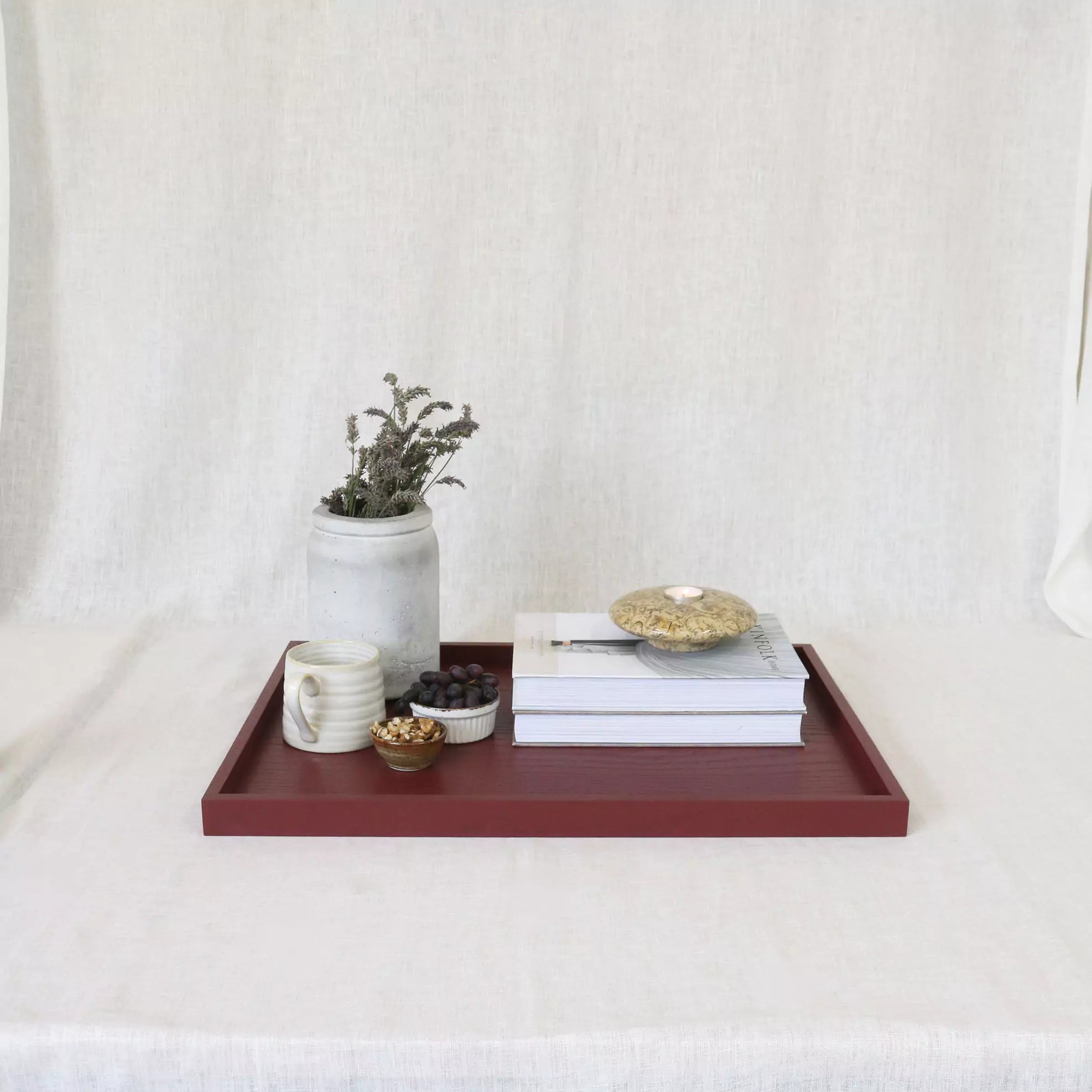 Wooden tray with decorative items including a mug, books, and a plant on a white surface.