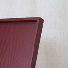 Wooden ottoman tray detail with a dark pink/red finish on a light grey background