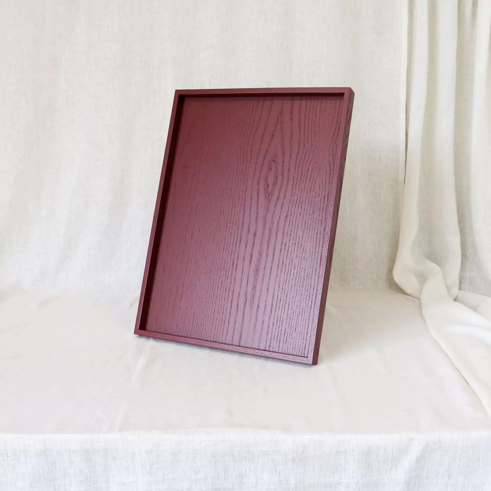 Wooden tray with a dark pink finish on a white fabric background