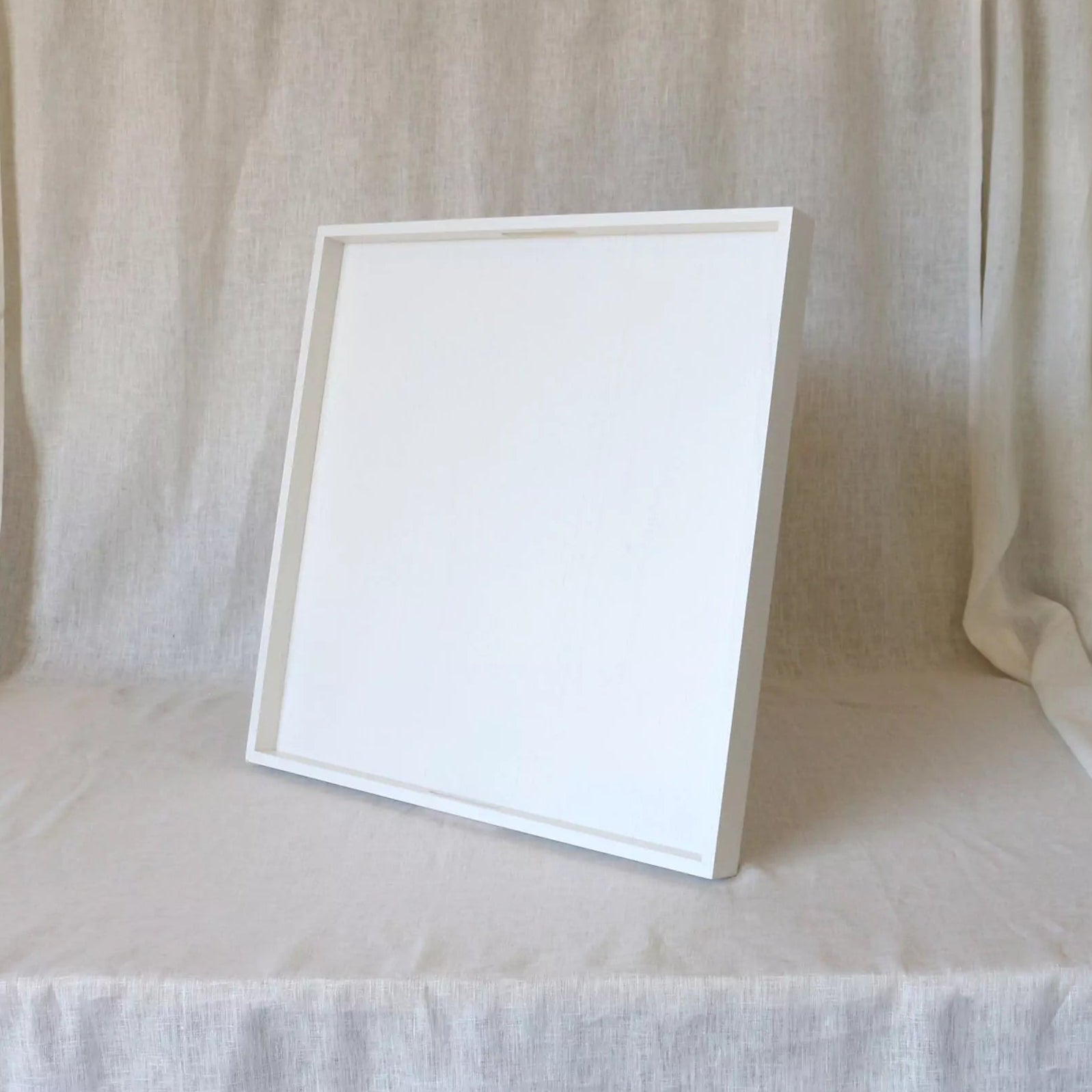 White ottoman tary with handles on a table with a white curtain in the background