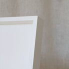 Close-up of a white ottoman tray frame corner on a beige wall.