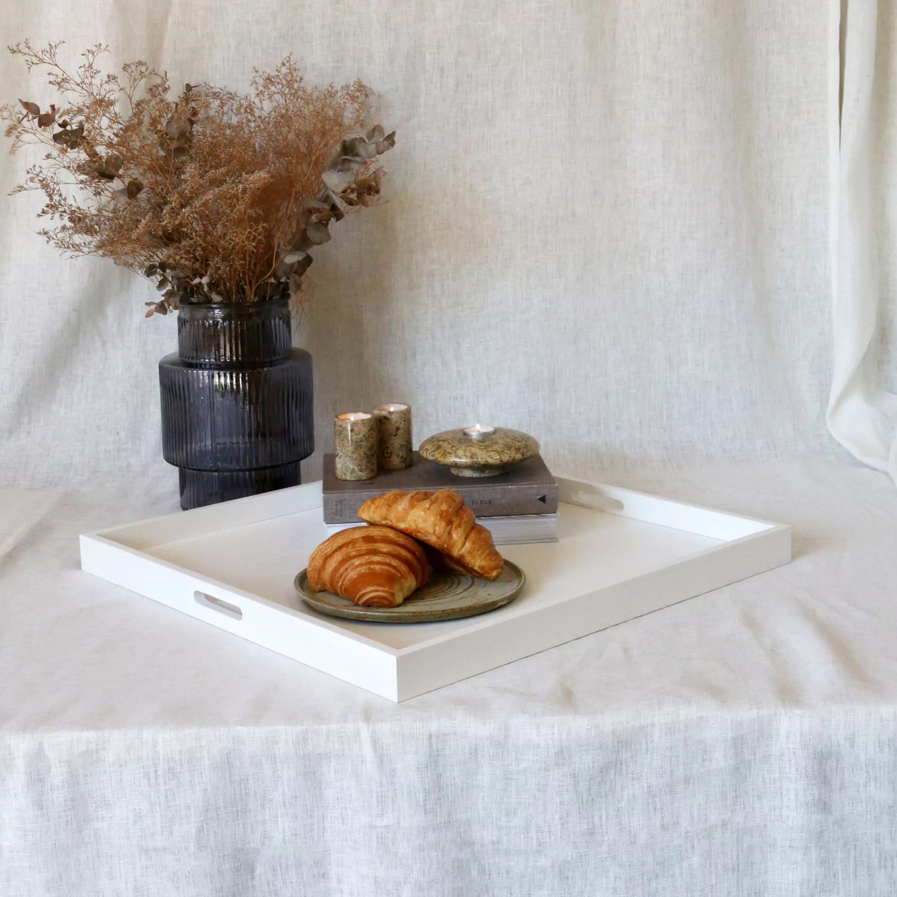 Tray with pastries and a vase of dried flowers on a white tablecloth.