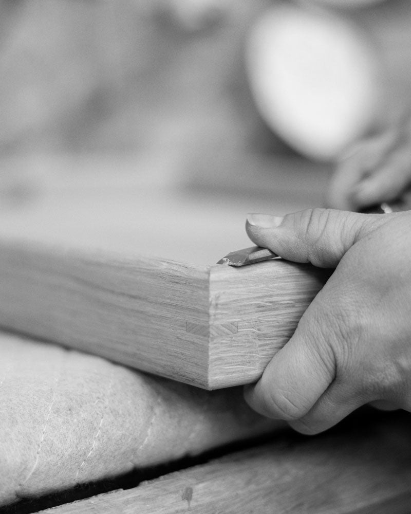 Close-up of a woodworker's hands carefully shaping the edge of a wooden tray using a chisel, highlighting fine craftsmanship.