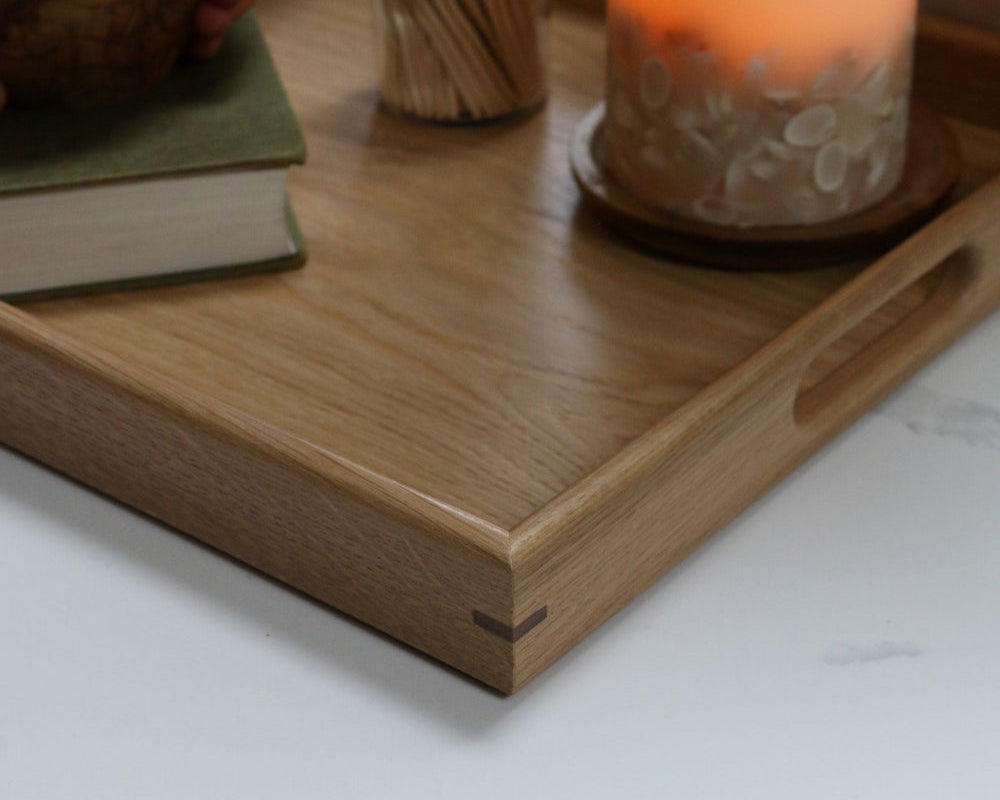 Detailed corner view of a wooden footstool tray, highlighting its smooth finish and precisely joined edges, accompanied by a candle and book.