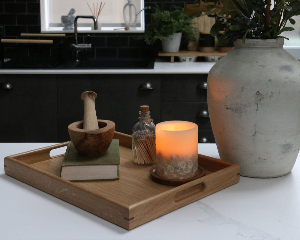 Handcrafted oak coffee table tray on a modern kitchen counter, decorated with a wooden mortar and pestle, a candle, and a glass jar of matches.