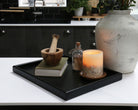 A decorative tray on a kitchen counter, styled with a candle, a book, and a wooden mortar and pestle, showcasing its versatility.