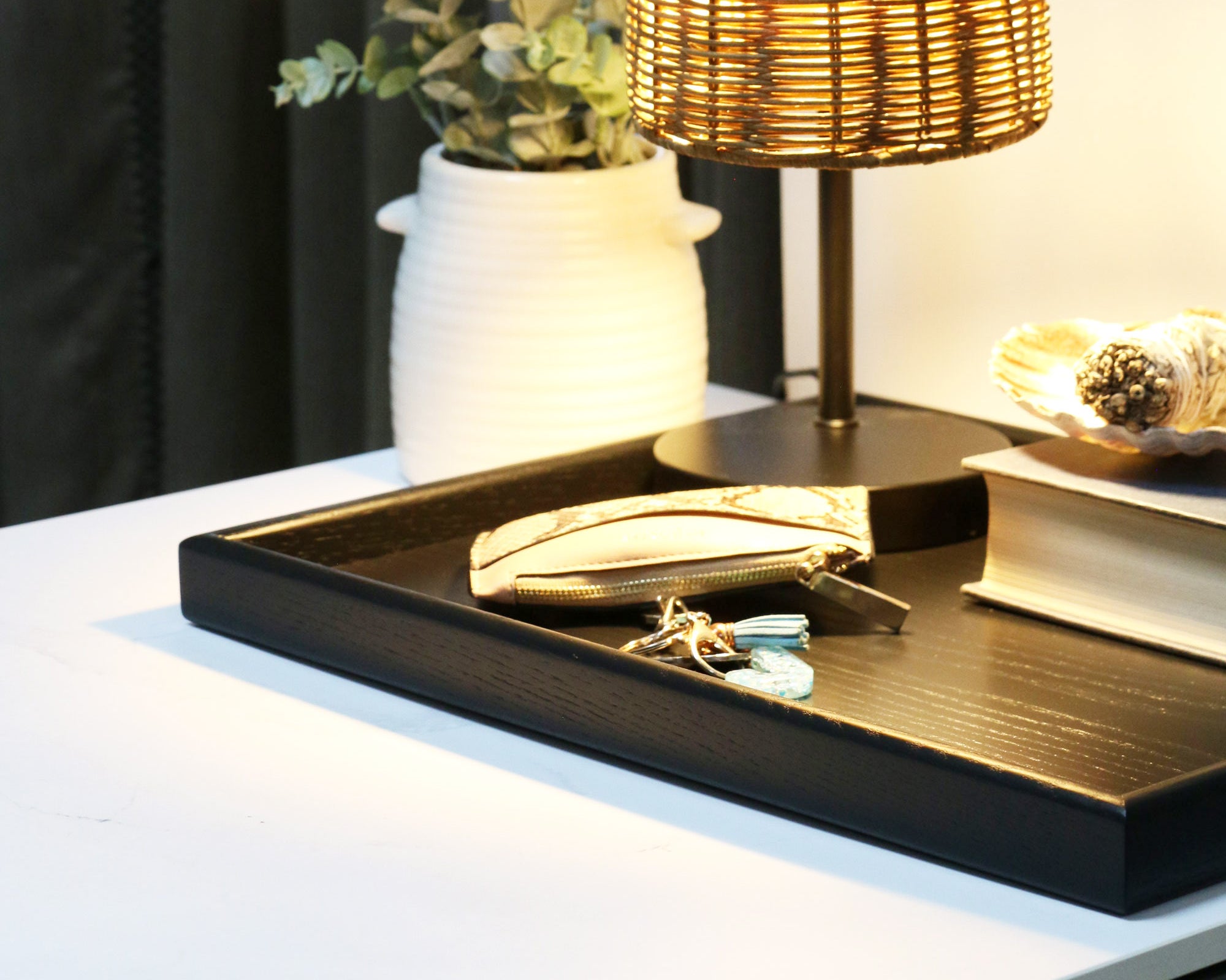 A decorative tray used as a stylish nightstand organizer, holding books, keys, and a lamp in a warm, ambient setting.