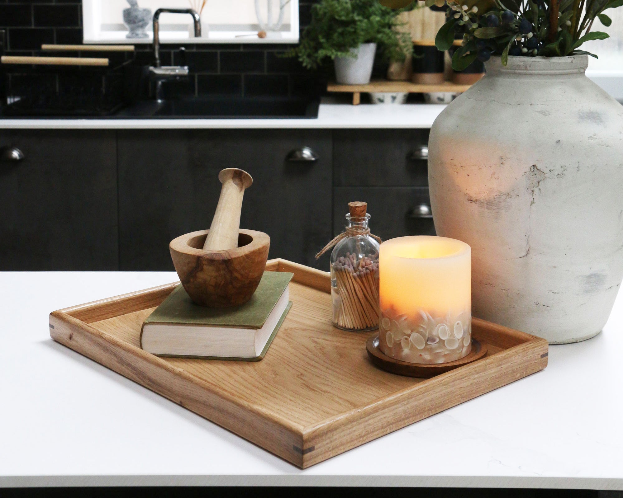 A decorative tray on a kitchen counter, styled with a candle, a book, and a wooden mortar and pestle, showcasing its versatility.