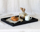 Coffee table tray in black wood, artistically arranged with a ceramic vase, cup, and napkin, showcasing its versatility as a decorative accent for living spaces.