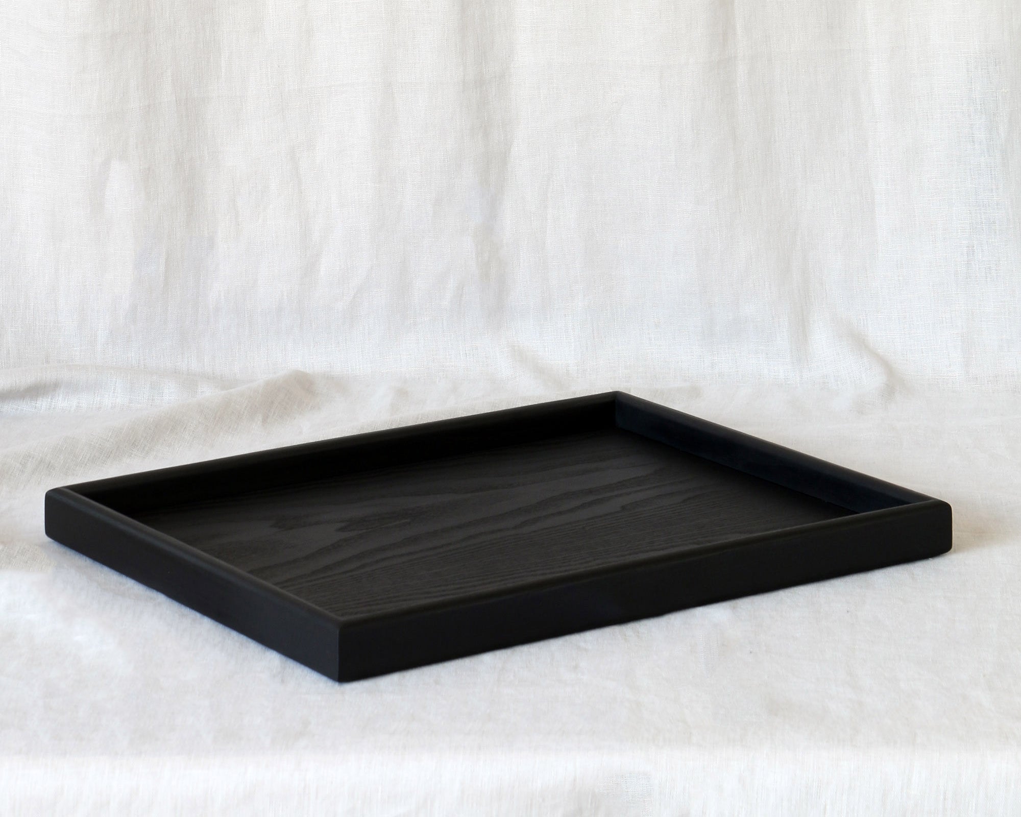 A coffee table tray in black wood, placed on a neutral fabric background, showing its elegant simplicity.