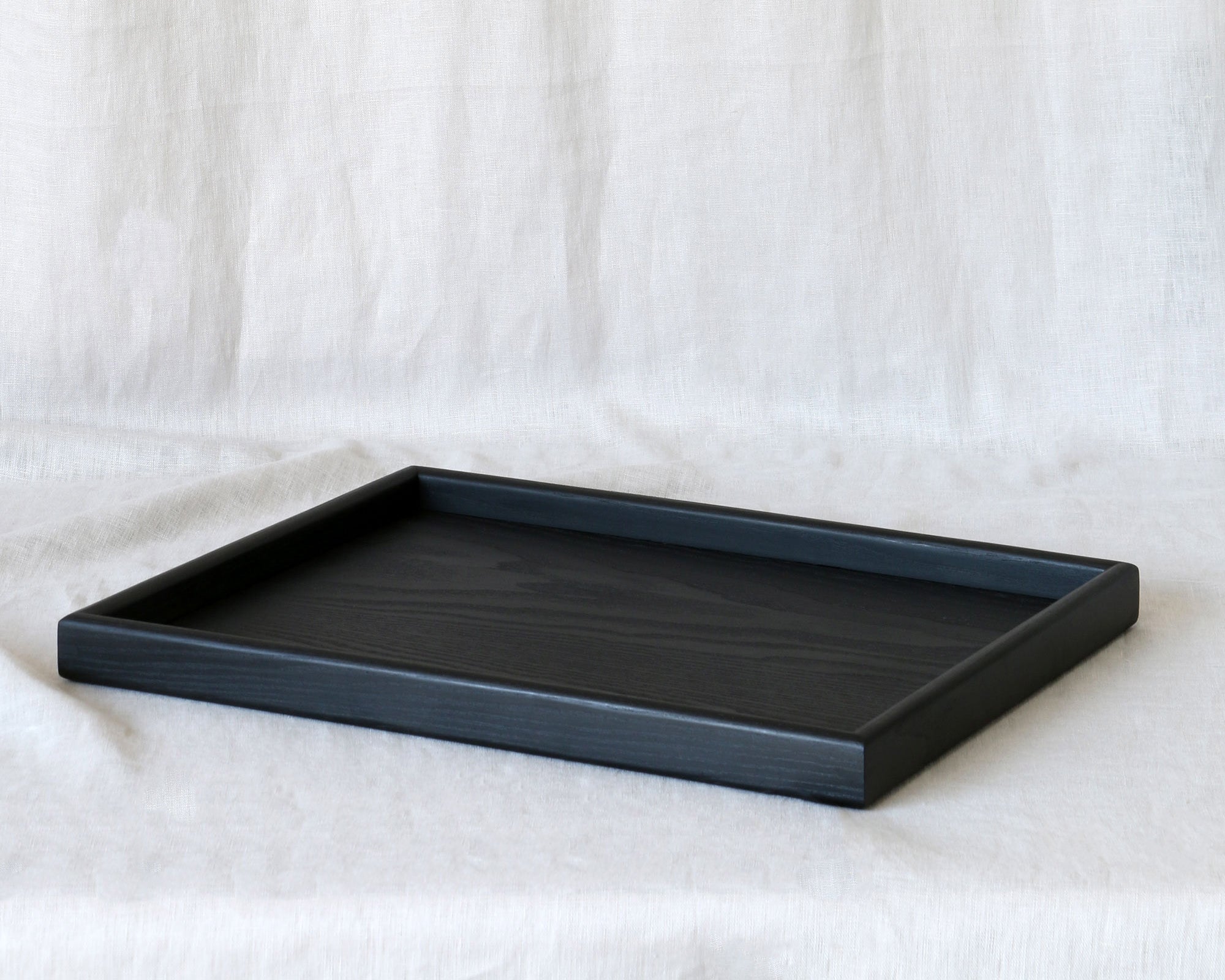 A black wooden tray for footstool, photographed at an angle, highlighting its raised edges and refined construction.