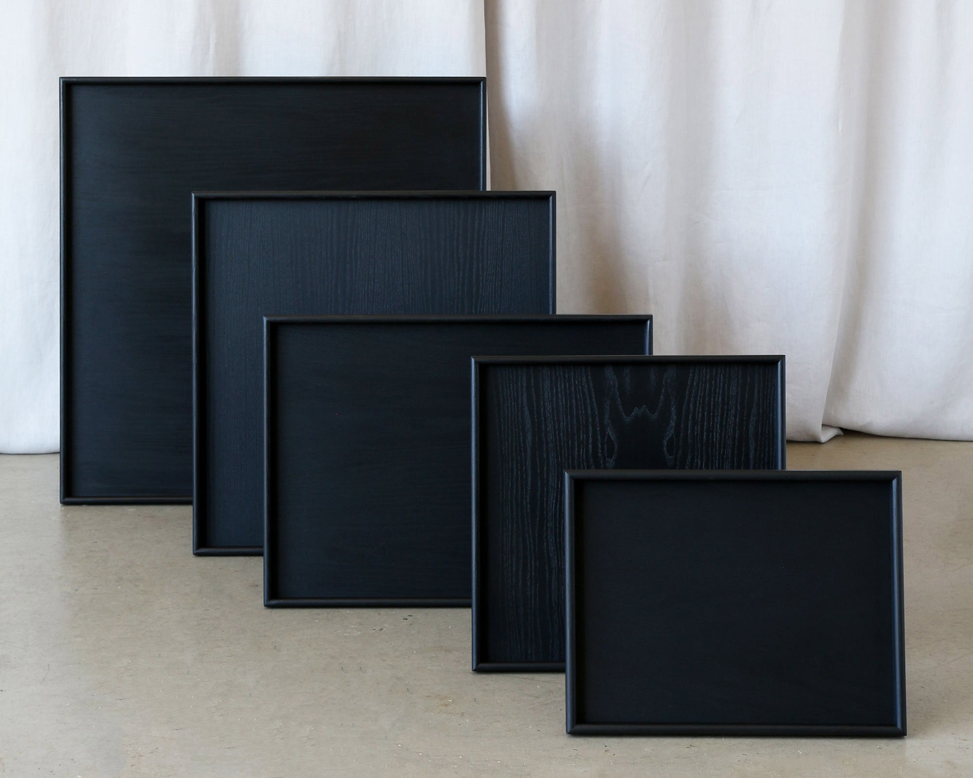 A set of handcrafted trays in black wood, displayed in multiple sizes, ideal as a wooden tray for footstool or coffee table tray.