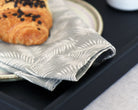 Decorative tray displaying intricate details of a napkin with delicate leaf prints placed on its surface, emphasizing the elegant craftsmanship.