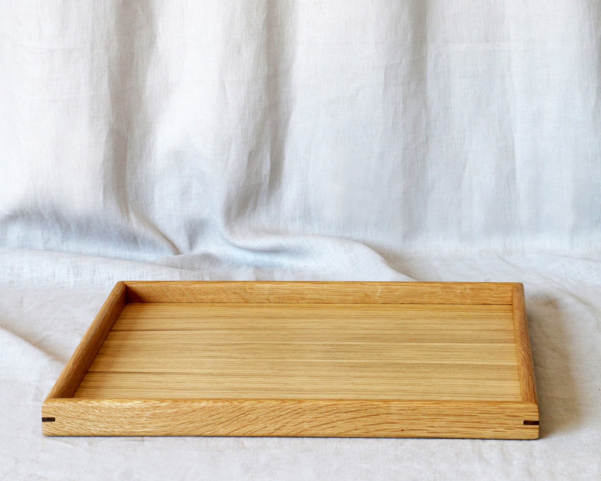 A medium-sized wooden tray for footstool, crafted from oak, displayed on a neutral fabric background.