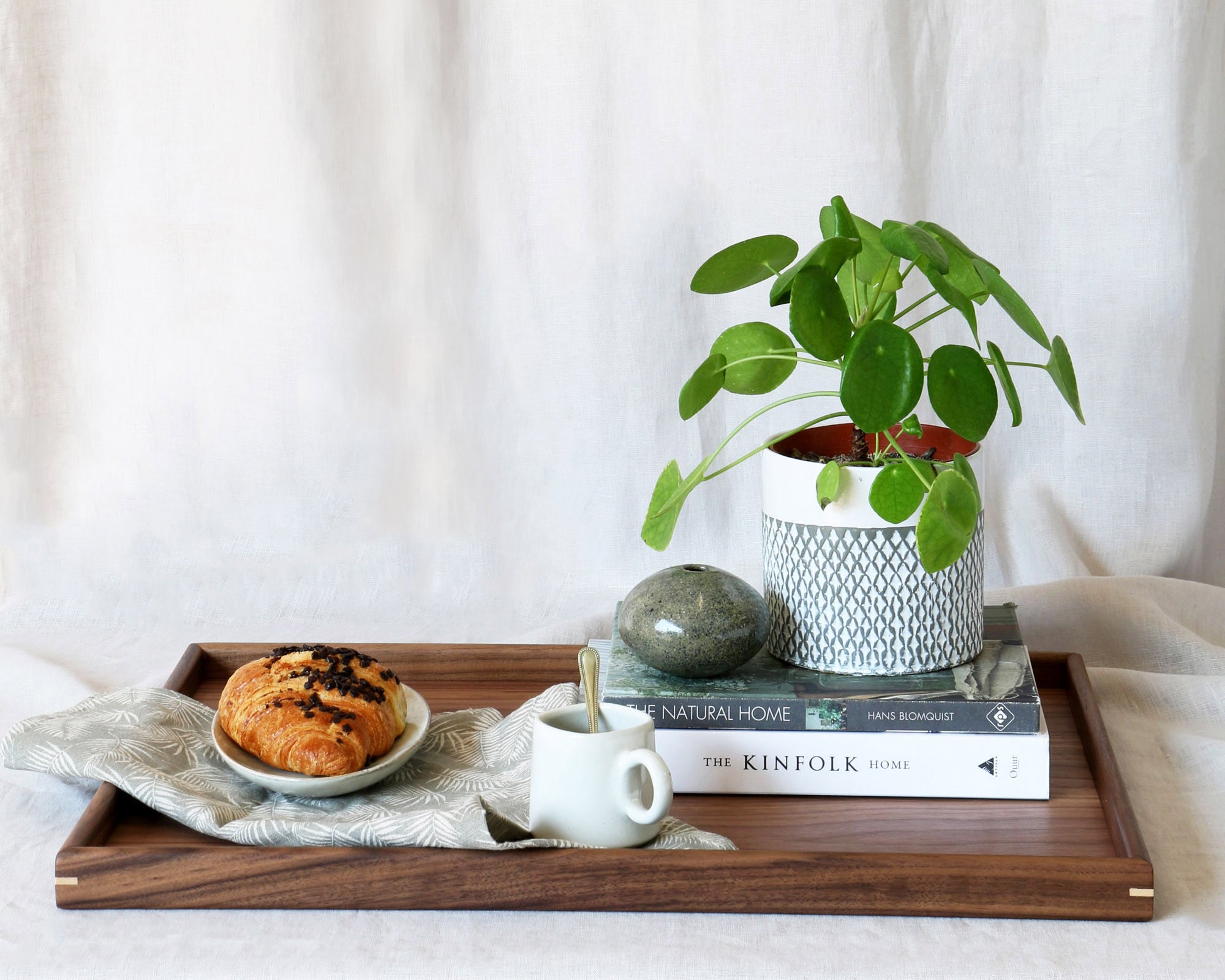 A decorative tray styled with books, a plant, and a pastry, showcasing its elegant functionality in a cozy setting.