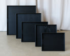 A set of handcrafted trays in black wood finish, neatly stacked in descending sizes against a neutral backdrop.