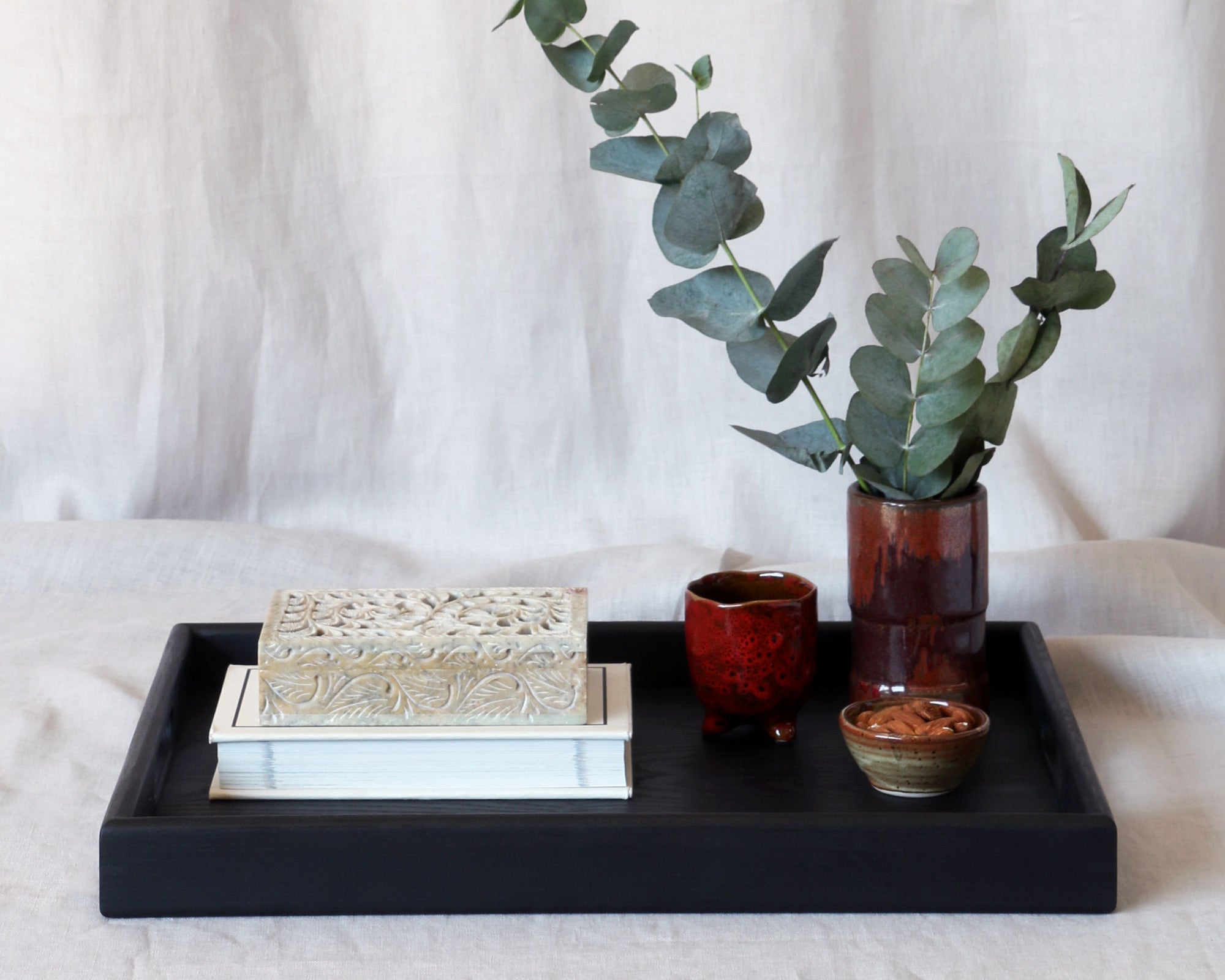 A decorative tray in black with books, a ceramic vase with eucalyptus, and artisanal pottery cups, styled elegantly.