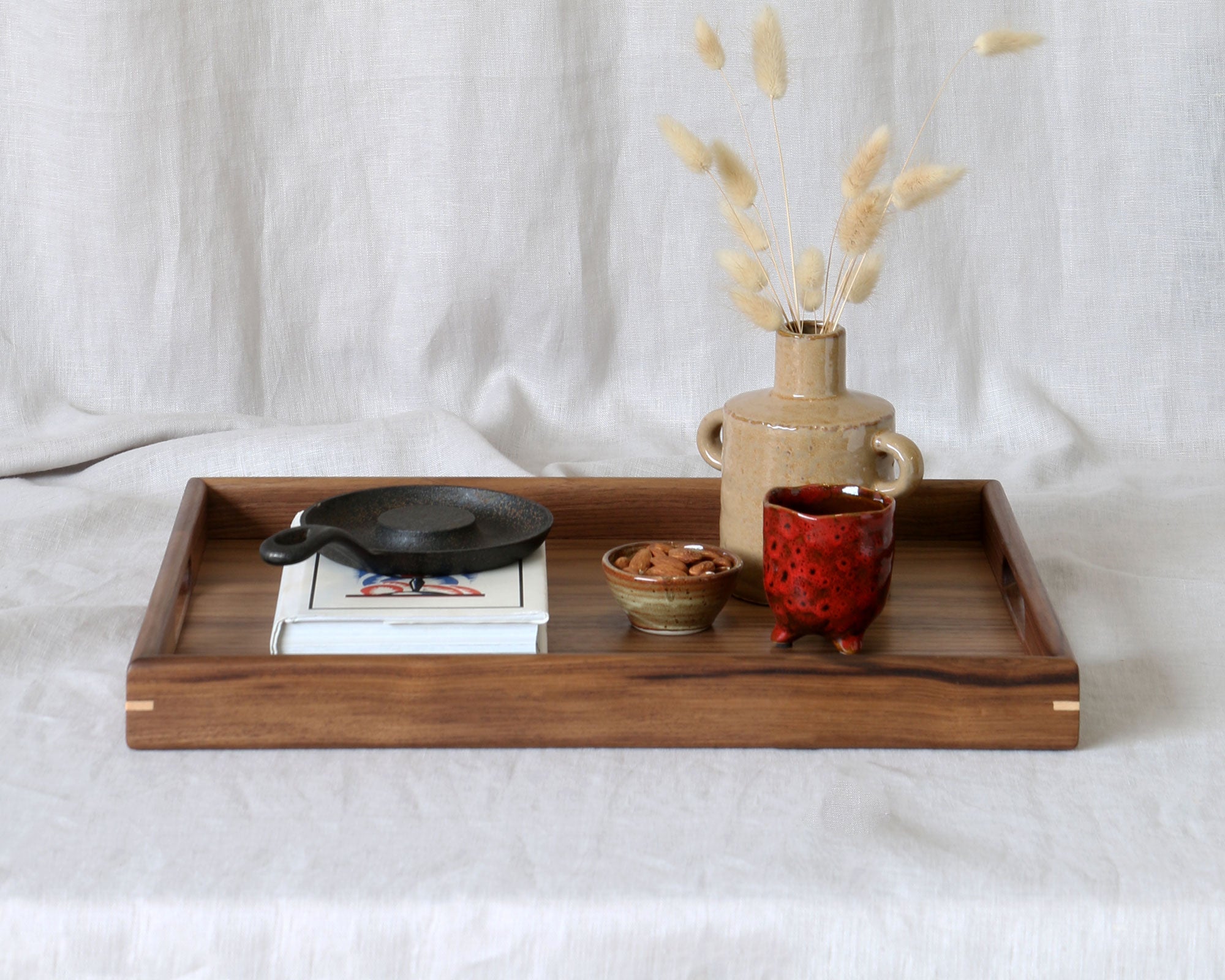 A walnut wooden ottoman tray adorned with artisanal objects, perfect for elegant home decor.