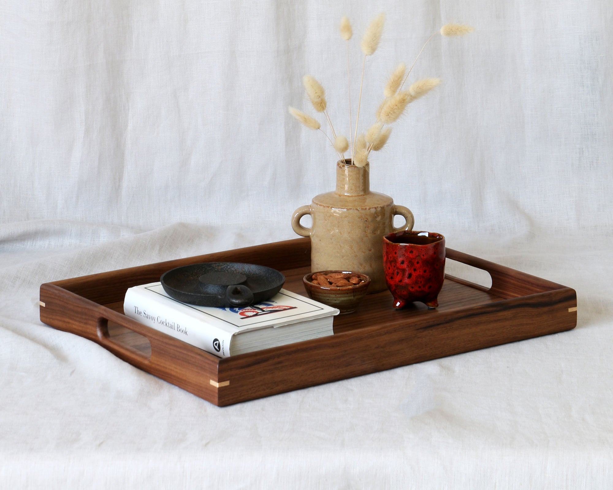 A handcrafted wooden tray with handles styled with books, ceramics, and dried flowers, making a sophisticated centerpiece.