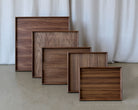 A set of five handcrafted wooden trays for footstools in rich walnut, arranged in descending sizes, showcasing their smooth finish and natural wood grain.