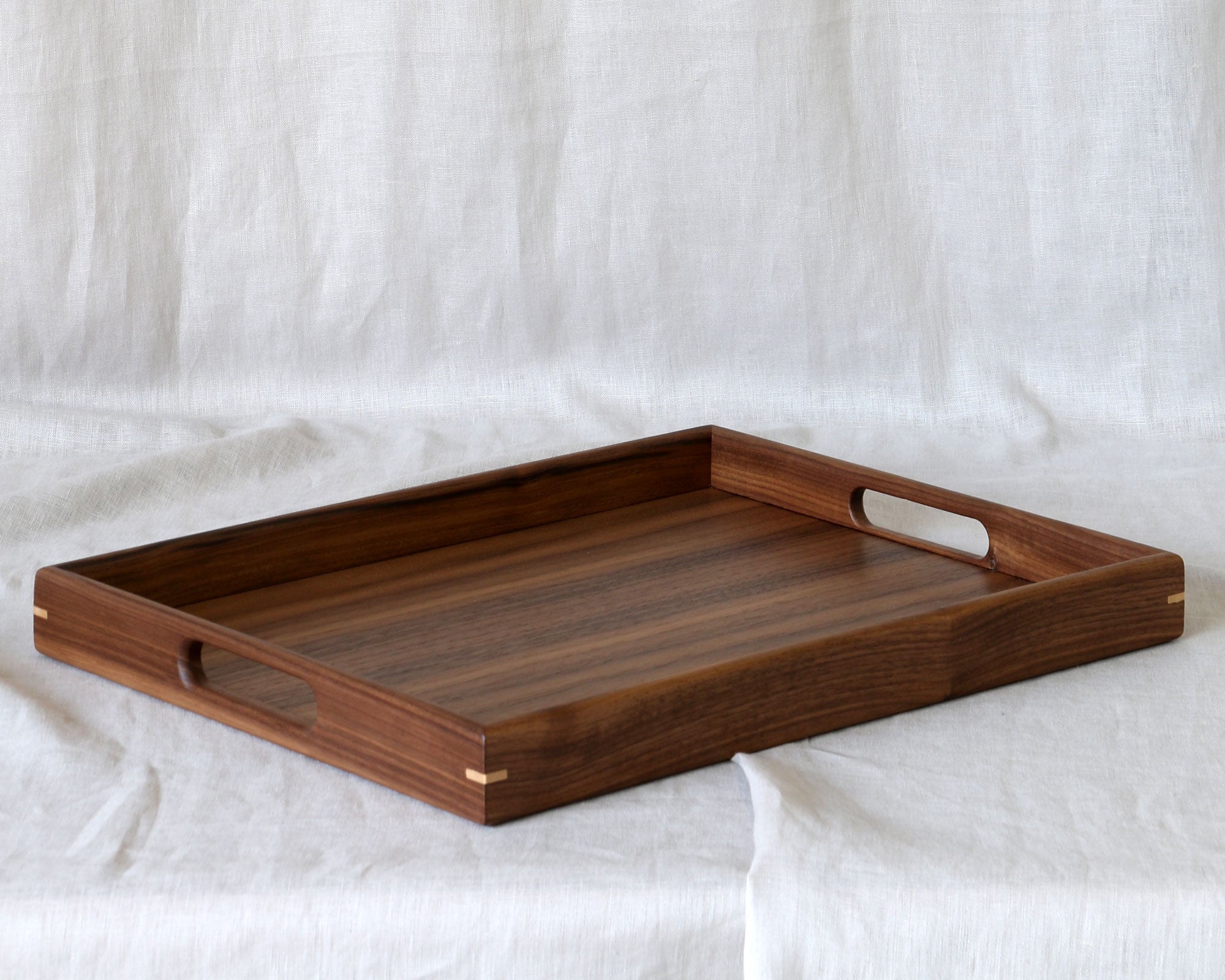 A decorative walnut serving tray with cut-out handles, set against a neutral fabric backdrop.