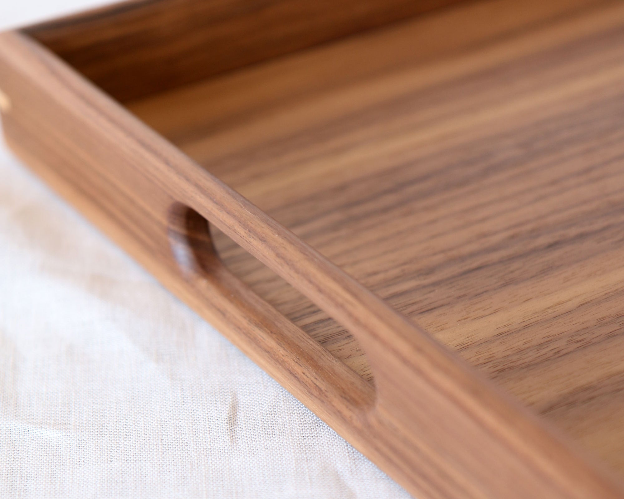 A close-up of a decorative tray in walnut, highlighting the precisely cut handle and fine craftsmanship.